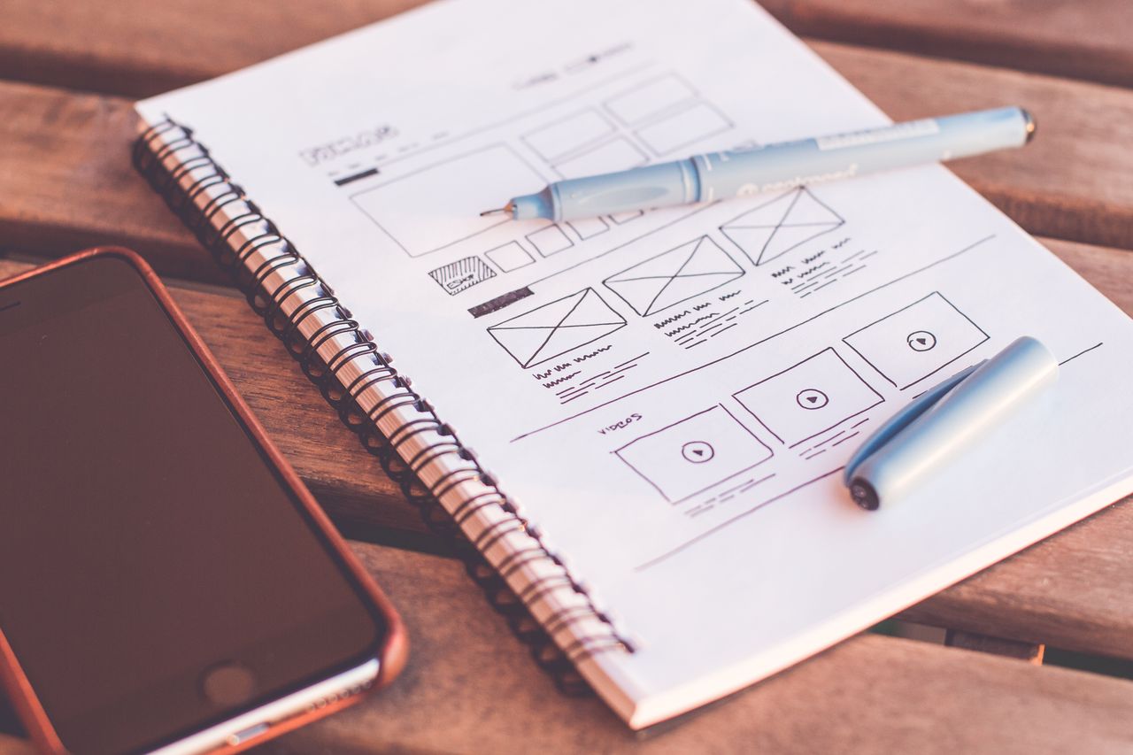 services-02 Gros plan d’un carnet présentant des esquisses de wireframes, accompagné d’un smartphone posé sur un bureau en bois.
